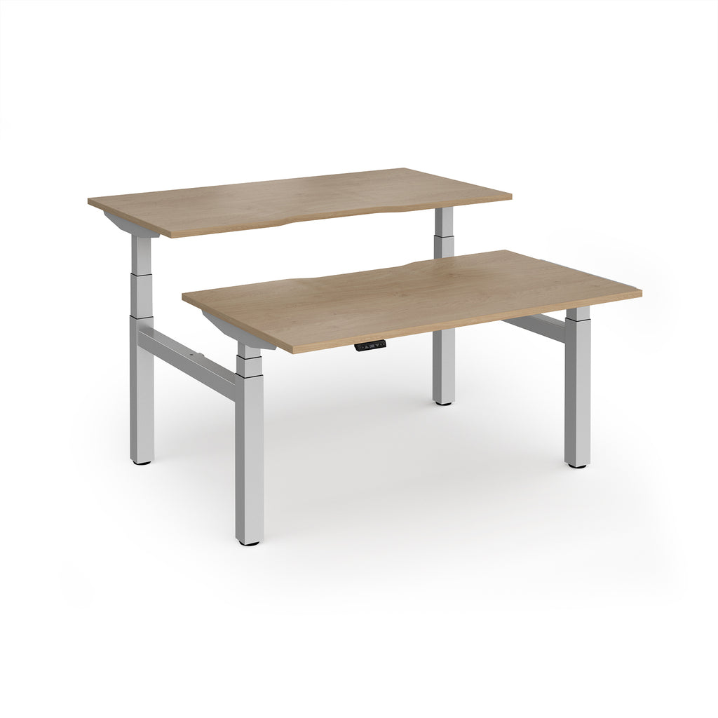 Two back-to-back height adjustable desks with shared silver metal frame and wood-effect tops on a white background