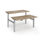 Two back-to-back height adjustable desks with shared silver metal frame and wood-effect tops on a white background