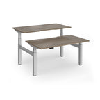 Two back-to-back height adjustable desks with shared silver metal frame and wood-effect tops on a white background