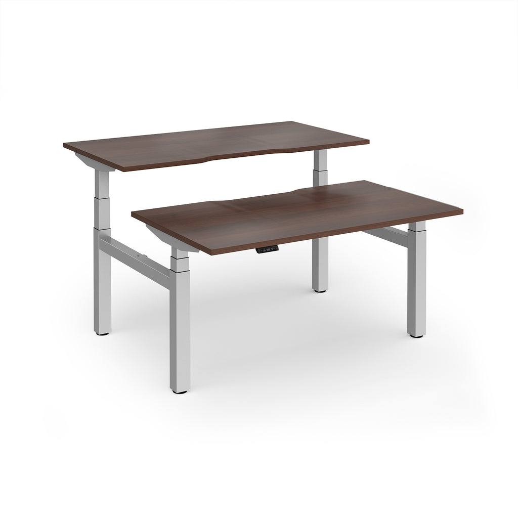 Two back-to-back height adjustable desks with shared silver metal frame and wood-effect tops on a white background