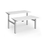 Two back-to-back height adjustable desks with shared silver metal frame and white tops on a white background