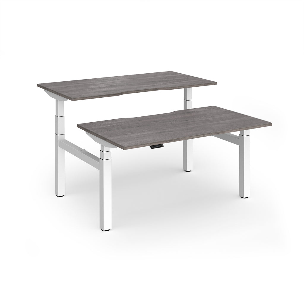 Two back-to-back height adjustable desks with shared white metal frame and grey wood-effect tops on a white background