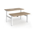 Two back-to-back height adjustable desks with shared white metal frame and wood-effect tops on a white background