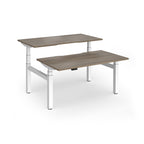 Two back-to-back height adjustable desks with shared white metal frame and wood-effect tops on a white background
