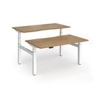 Two back-to-back height adjustable desks with shared white metal frame and wood-effect tops on a white background