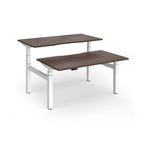 Two back-to-back height adjustable desks with shared white metal frame and wood-effect tops on a white background