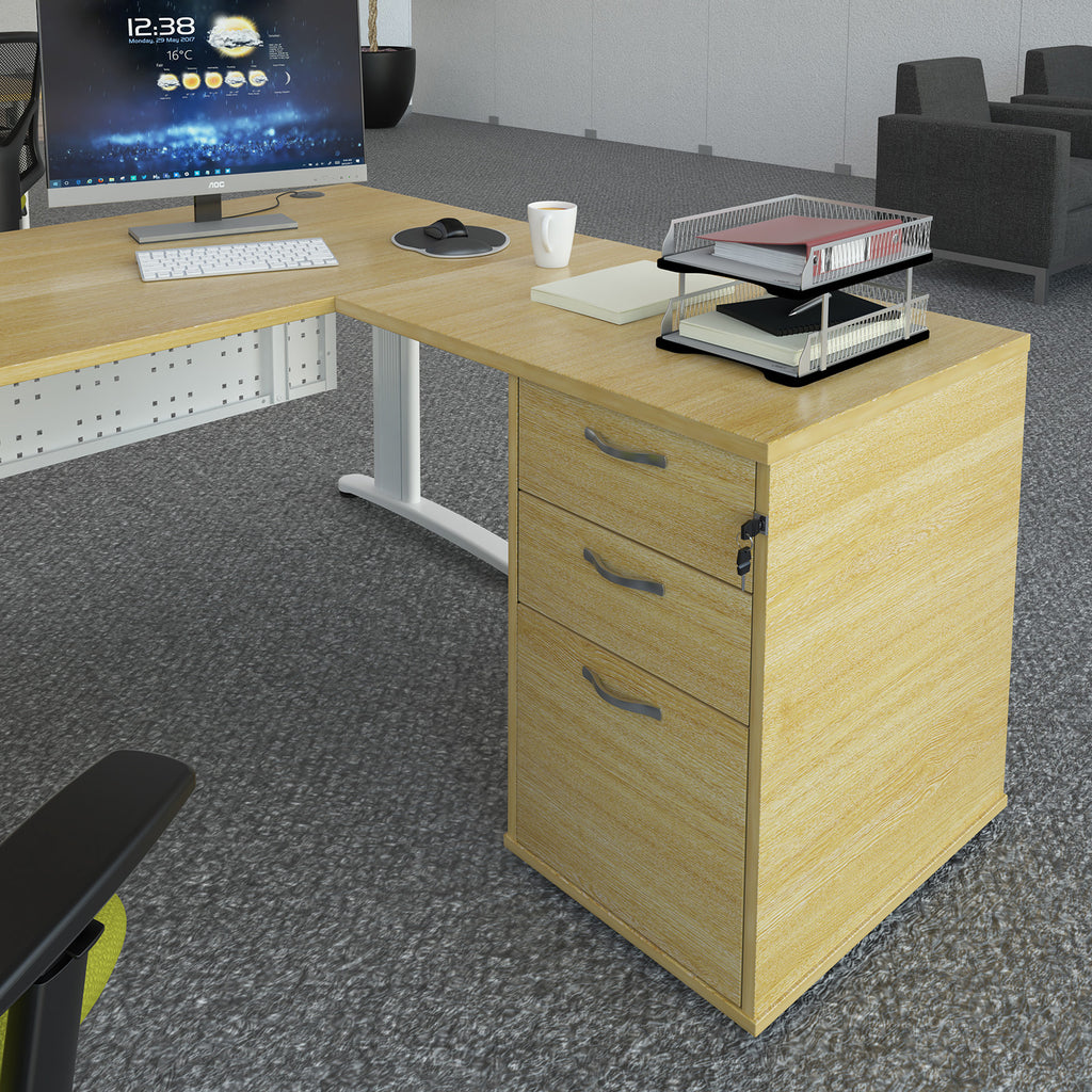 Desk extension with a light wood-effect finish, integrated three-drawer pedestal, and overhanging worktop, shown attached to a matching office desk in a modern office setting.