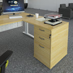 Desk extension with a light wood-effect finish, integrated three-drawer pedestal, and overhanging worktop, shown attached to a matching office desk in a modern office setting.