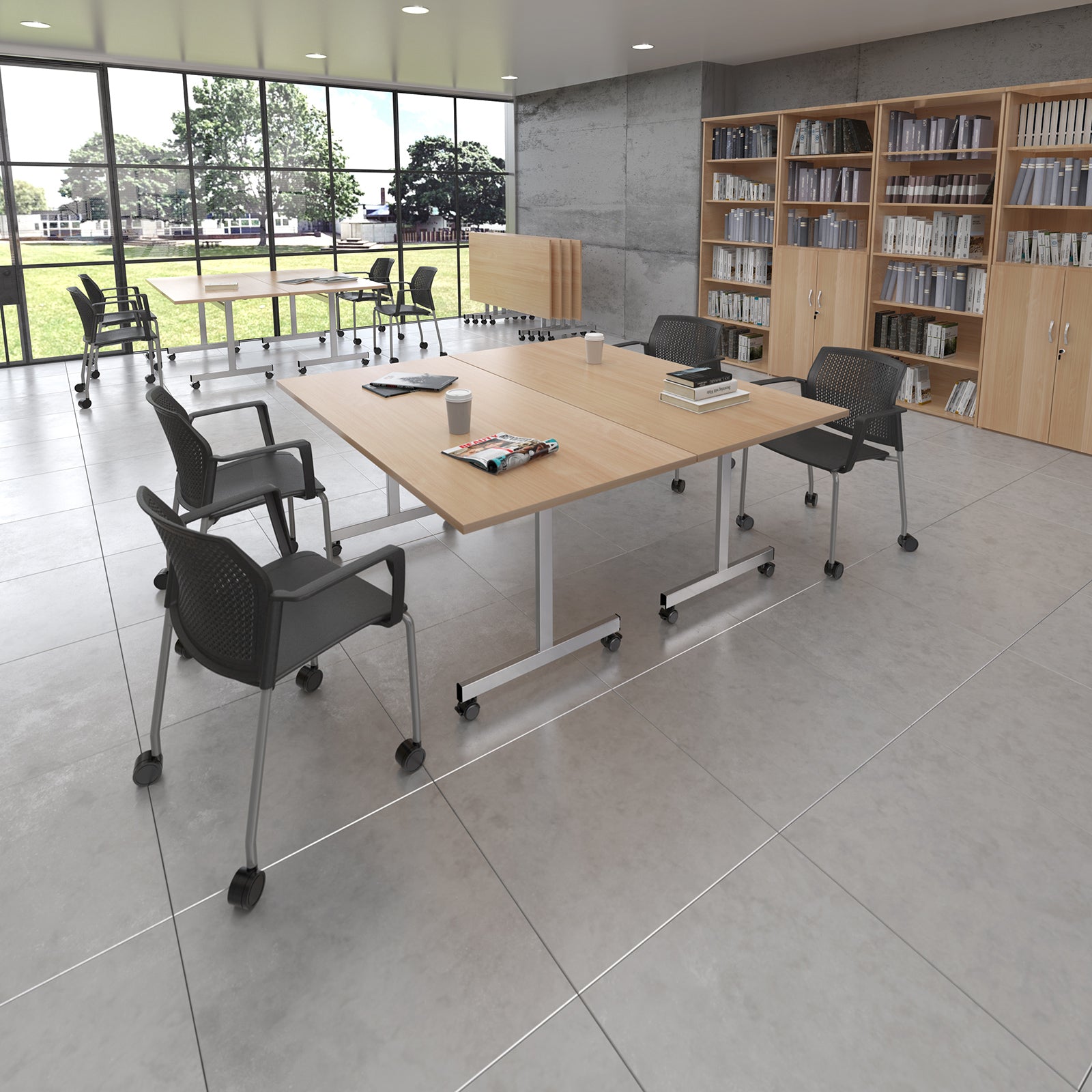 A modern office meeting room with a light wood rectangular conference table on casters, surrounded by black mesh office chairs with silver metal legs. Large windows on the left look out onto a green field, and light wood bookshelves line the right wall.