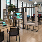 A modern office modular storage wall with a black metal frame, light wood shelves, built-in storage, a bench seat, and a mounted TV screen, shown in a bright office interior.