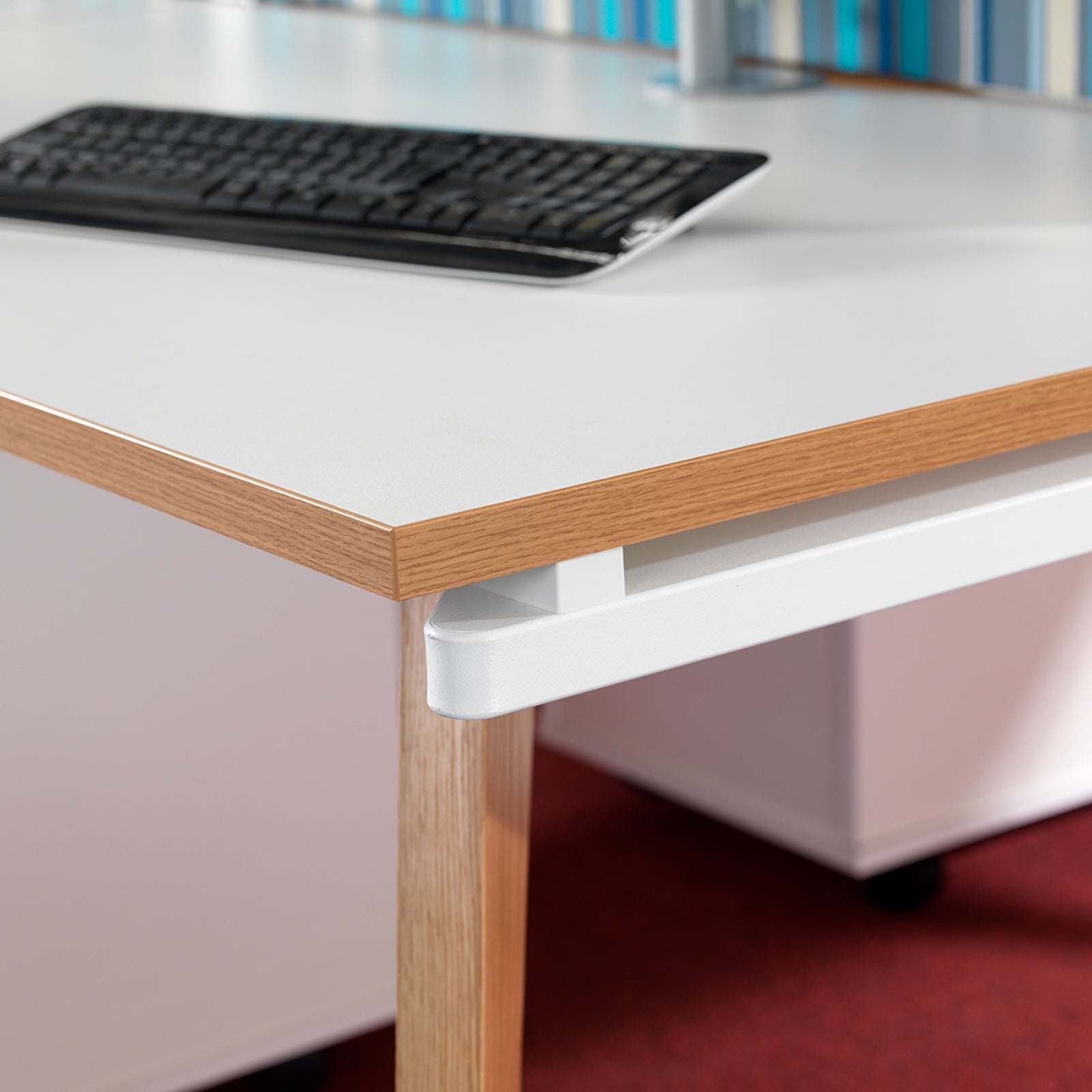White desk with wooden legs and a black keyboard on a blurred office background