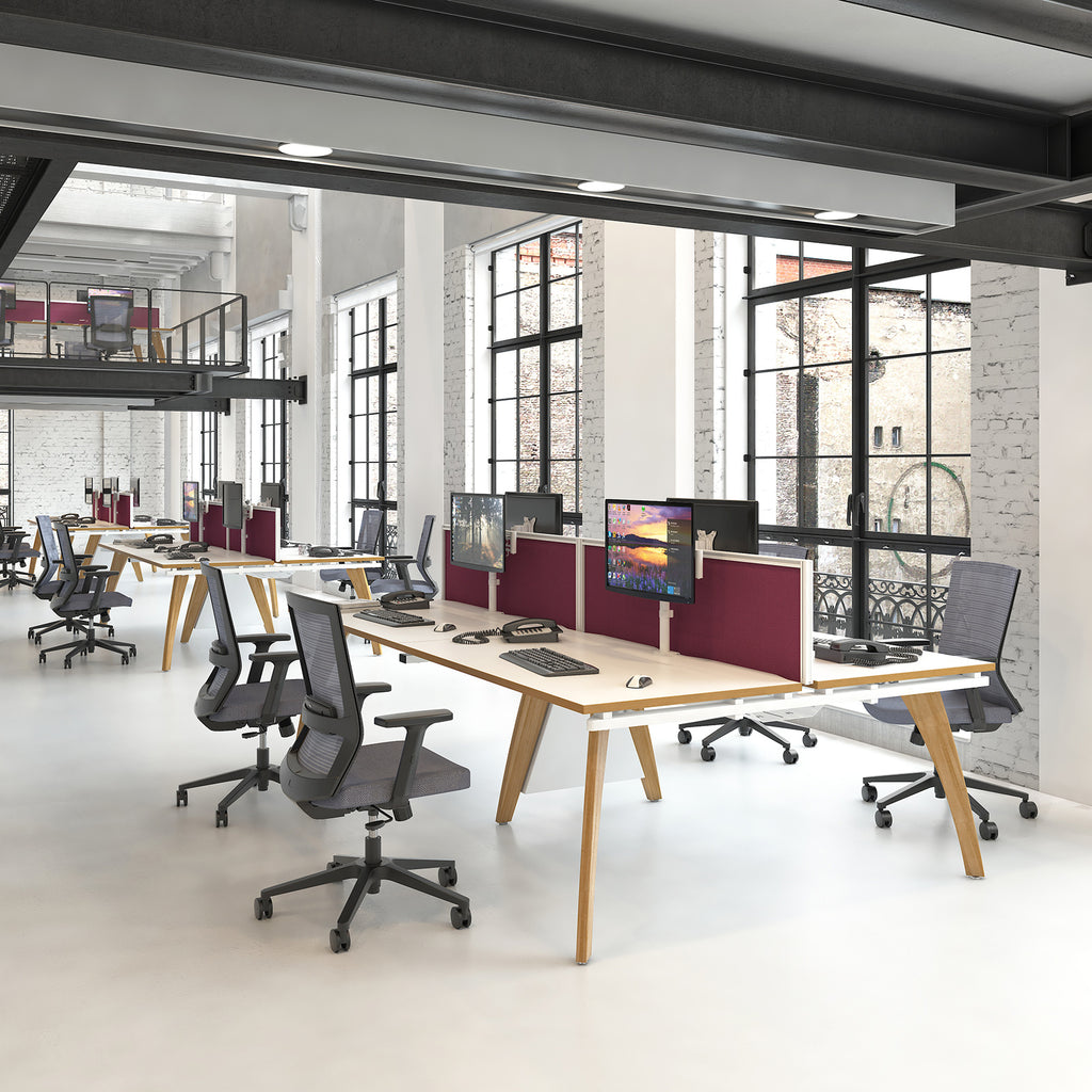 Modern open-plan office with shared bench desks, ergonomic task chairs, desk-mounted screens, and burgundy desk divider panels, set in a bright industrial-style workspace with large windows.