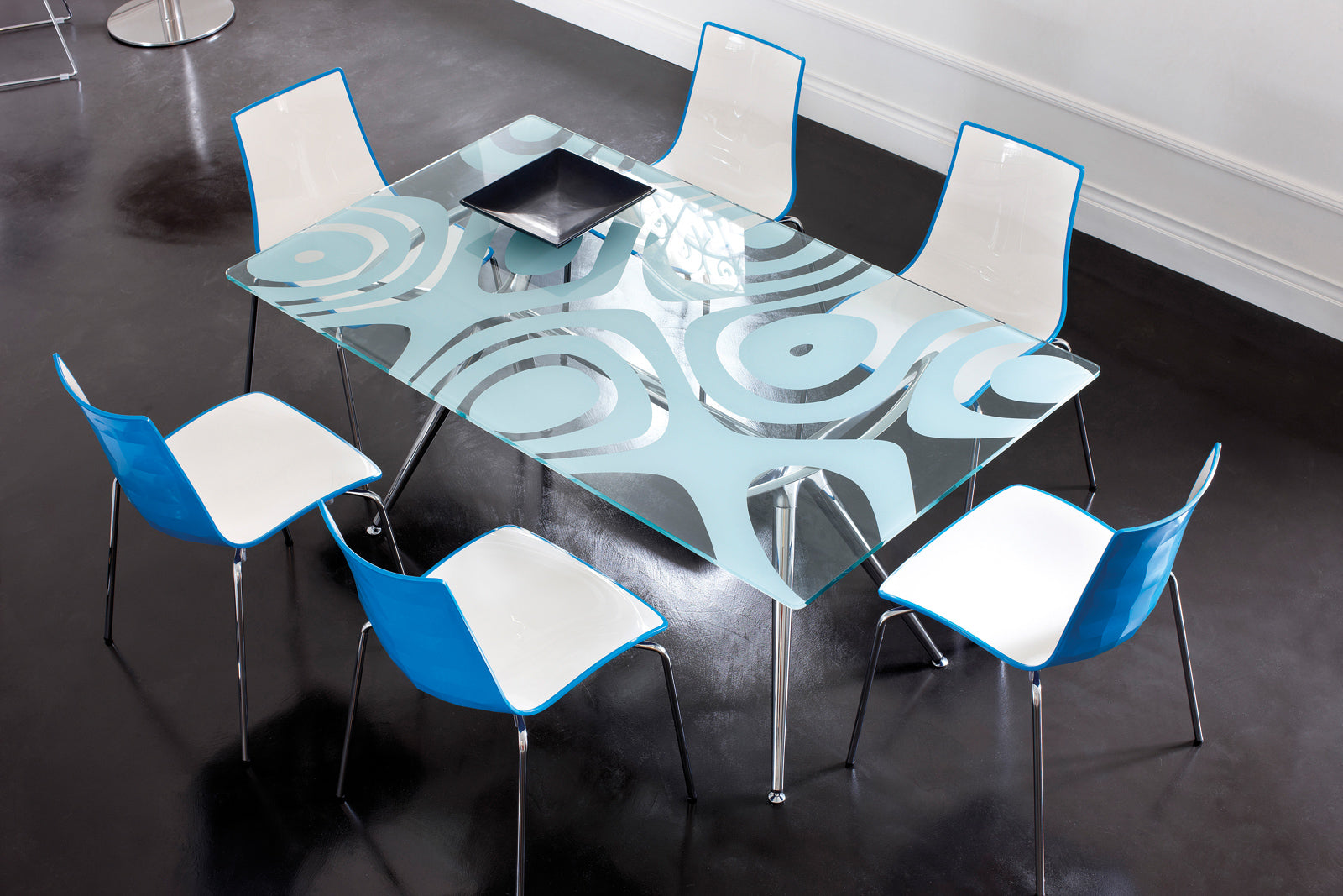 Modern glass dining table with decorative pattern surrounded by chairs in a stylish interior setting.