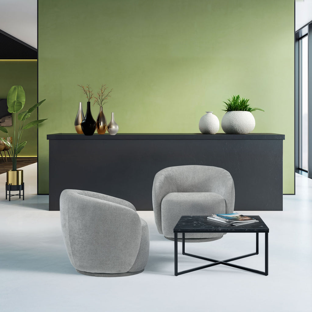 Modern interior with grey armchairs, a black coffee table, and decorative items against a green wall.