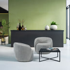 Modern interior with grey armchairs, a black coffee table, and decorative items against a green wall.