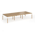 Triple back to back desk with light oak wood grain top and legs with white frame on a white background