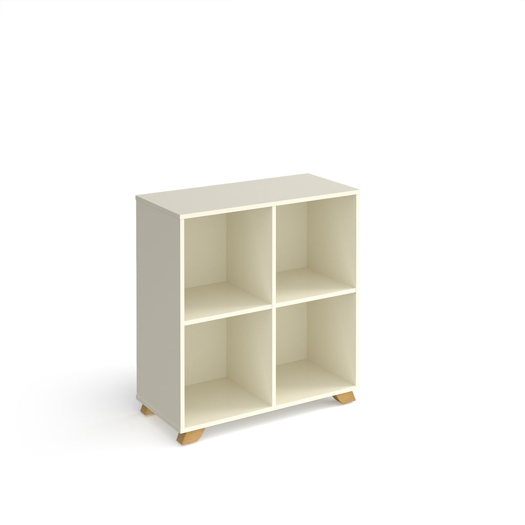 A modern 4-compartment cube storage shelf in a warm off-white finish with small natural wood feet, shown on a plain white background.