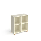 A modern 4-compartment cube storage shelf in a warm off-white finish with small natural wood feet, shown on a plain white background.