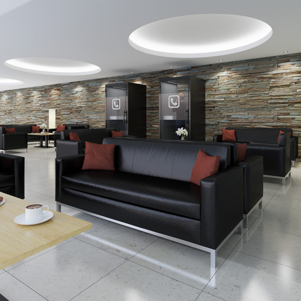 Modern lounge area with black leather couches and red pillows against a stone wall.