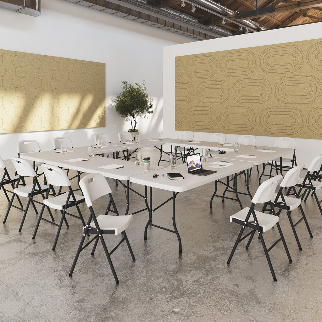 Modern office space with white tables and chairs, decorative wall panels, and a plant.