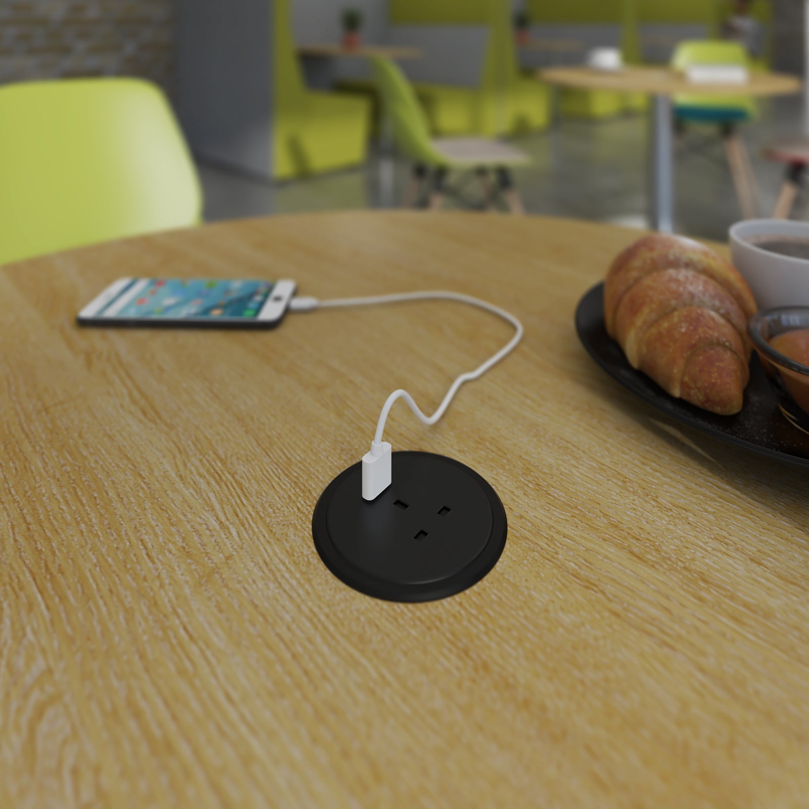 A round black table outlet socket on a light wood table, with a white charging cable plugged in and a smartphone nearby in a café setting.