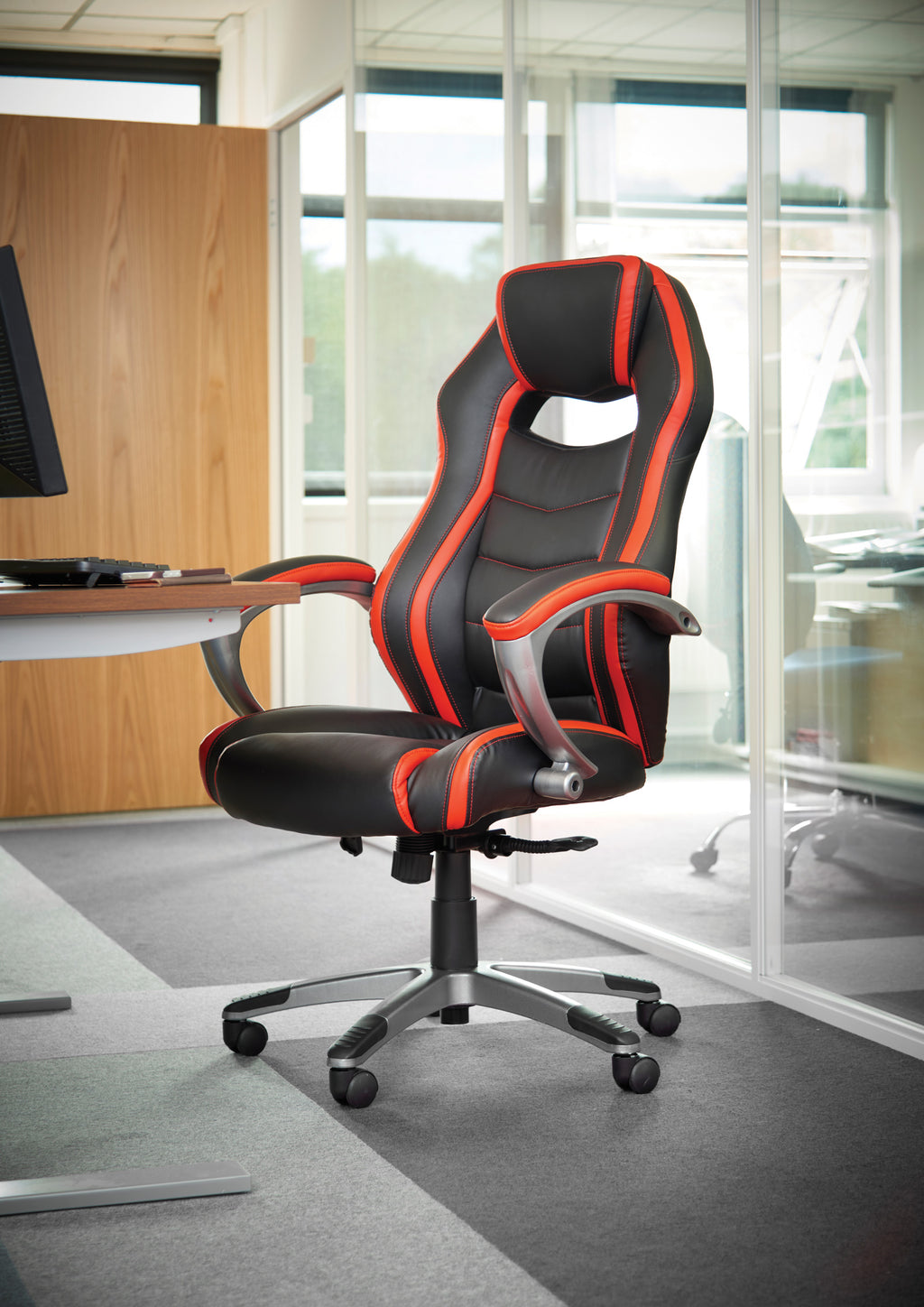 Black and red office chair in an office setting with a desk and large windows.