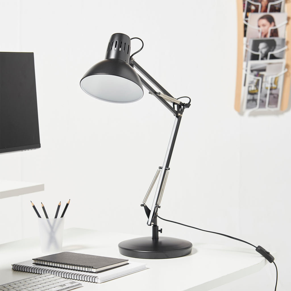 Black adjustable desk lamp on a white desk with office supplies.
