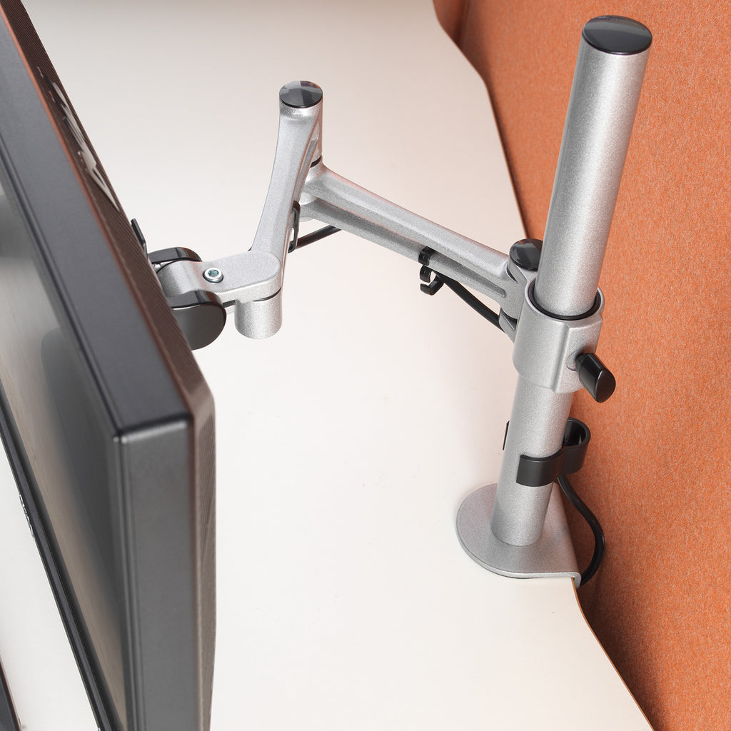 Monitor stand attached to a desk with a computer monitor on a white surface.