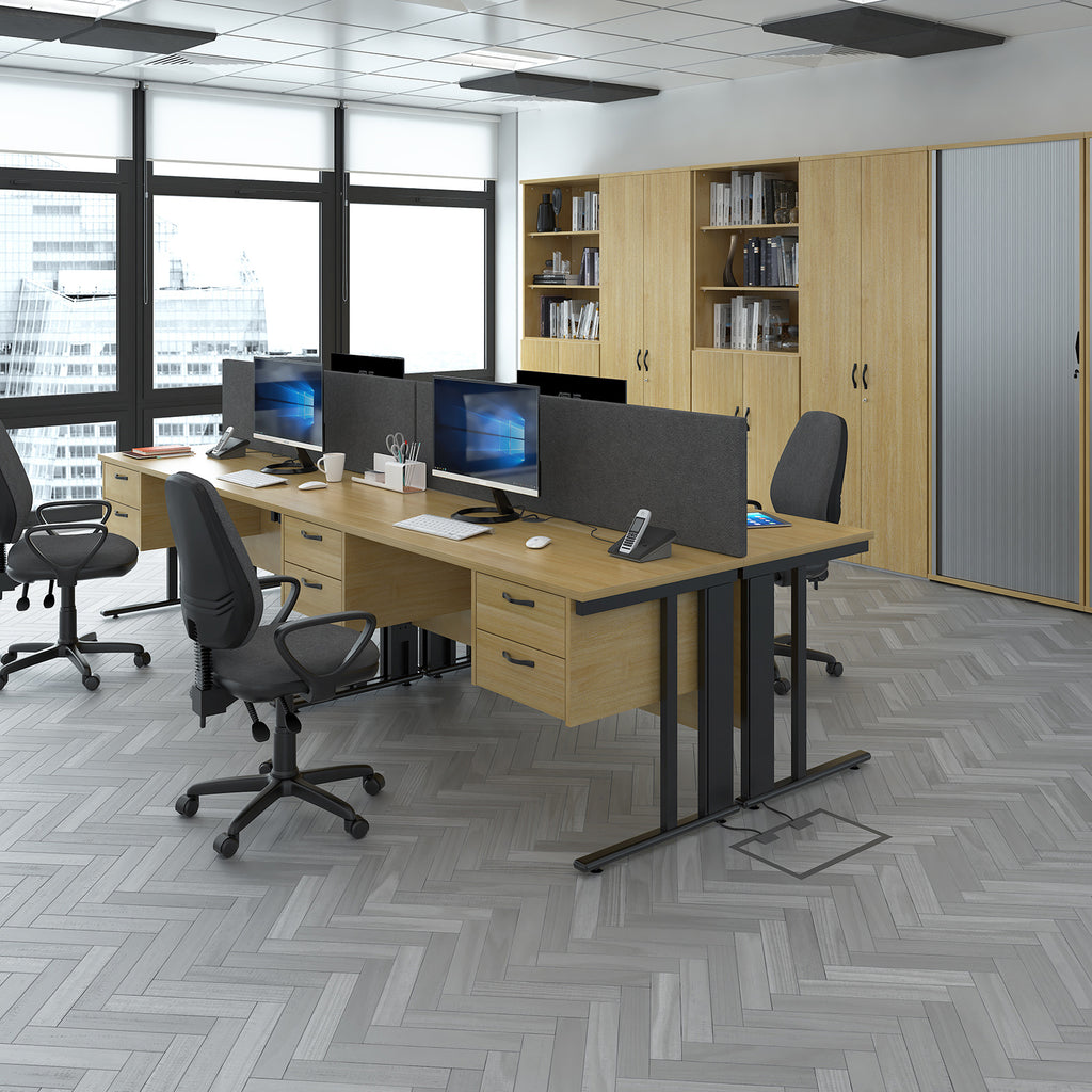 Modern open-plan office with wooden desks, ergonomic chairs, desktop computers, storage cabinets, and large windows letting in natural light.