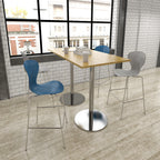 Modern cafe interior with a wooden table and colorful chairs against a brick wall.
