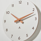 White wall clock with wooden hands on a light grey background