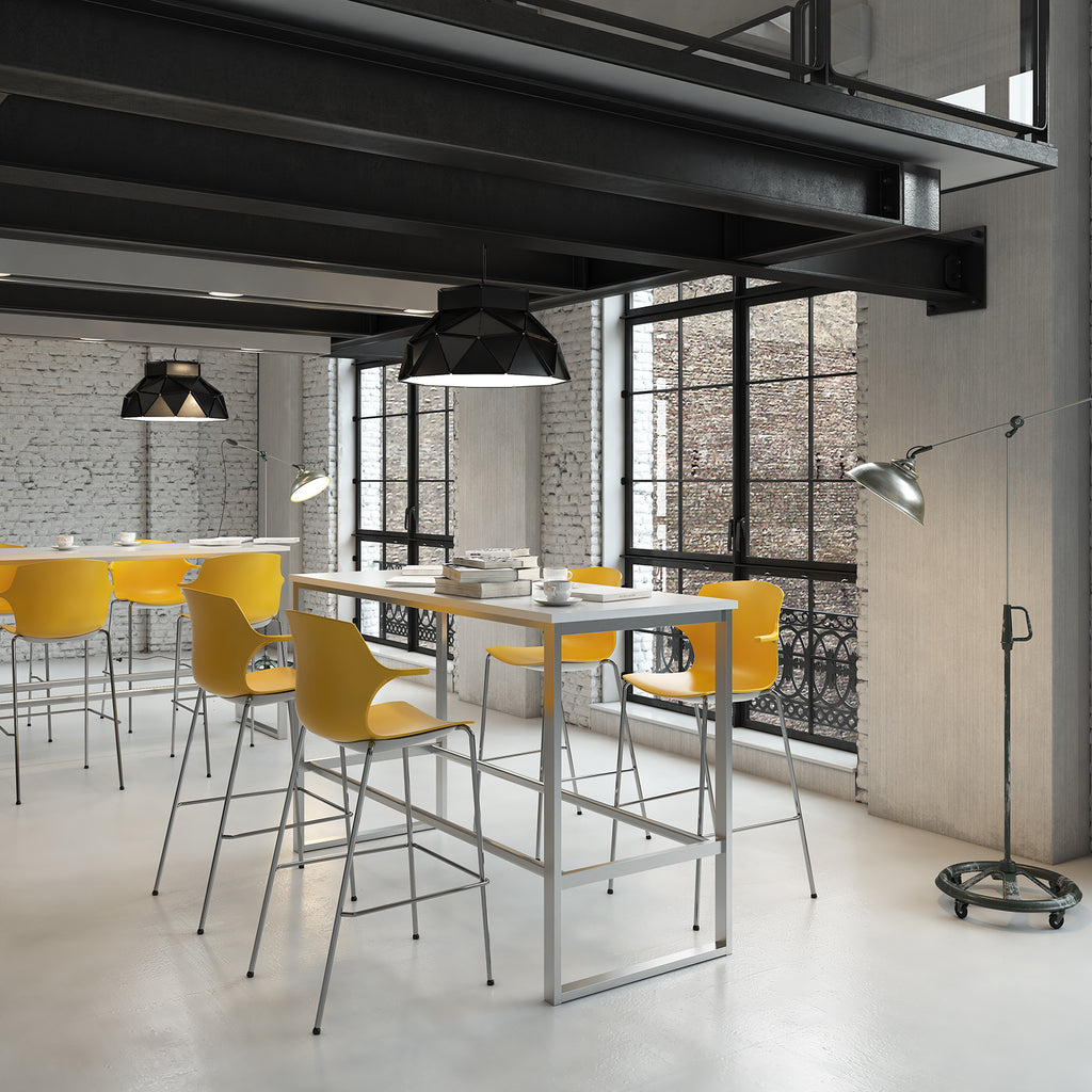 High table with a light grey top and metal frame, paired with yellow bar stools, shown in an industrial-style breakout and collaboration space.