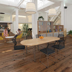 Modern office space with a long wooden table and chairs, bookshelves, and people sitting.