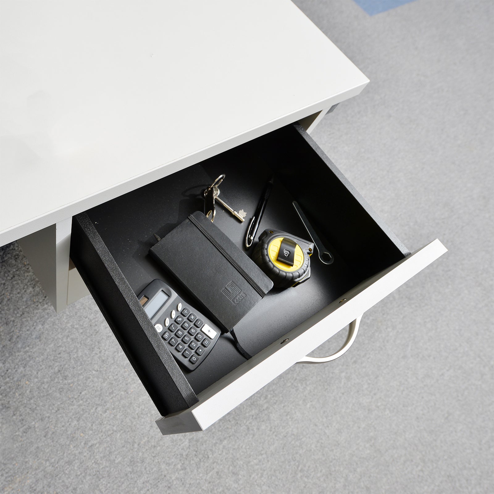 Open desk drawer with office supplies including a calculator and tape measure.