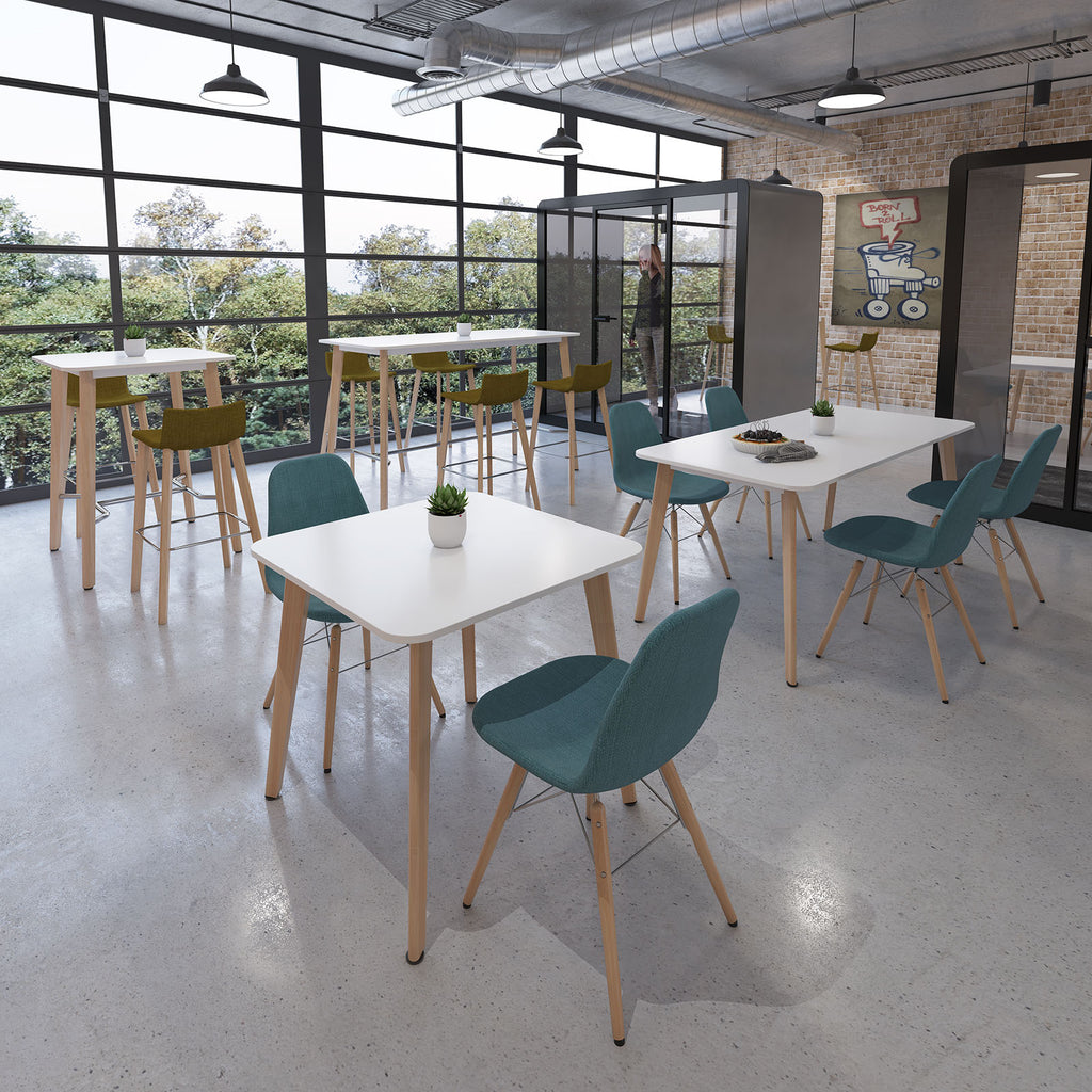 Contemporary office breakout space with white tables, upholstered chairs, high benches, and large windows creating a bright, relaxed setting.