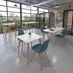 Contemporary office breakout space with white tables, upholstered chairs, high benches, and large windows creating a bright, relaxed setting.