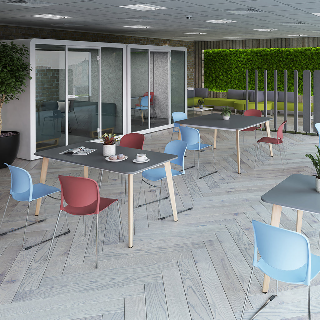 Contemporary office breakout area with café-style tables, colourful chairs, meeting pods, and green wall seating for informal collaboration.