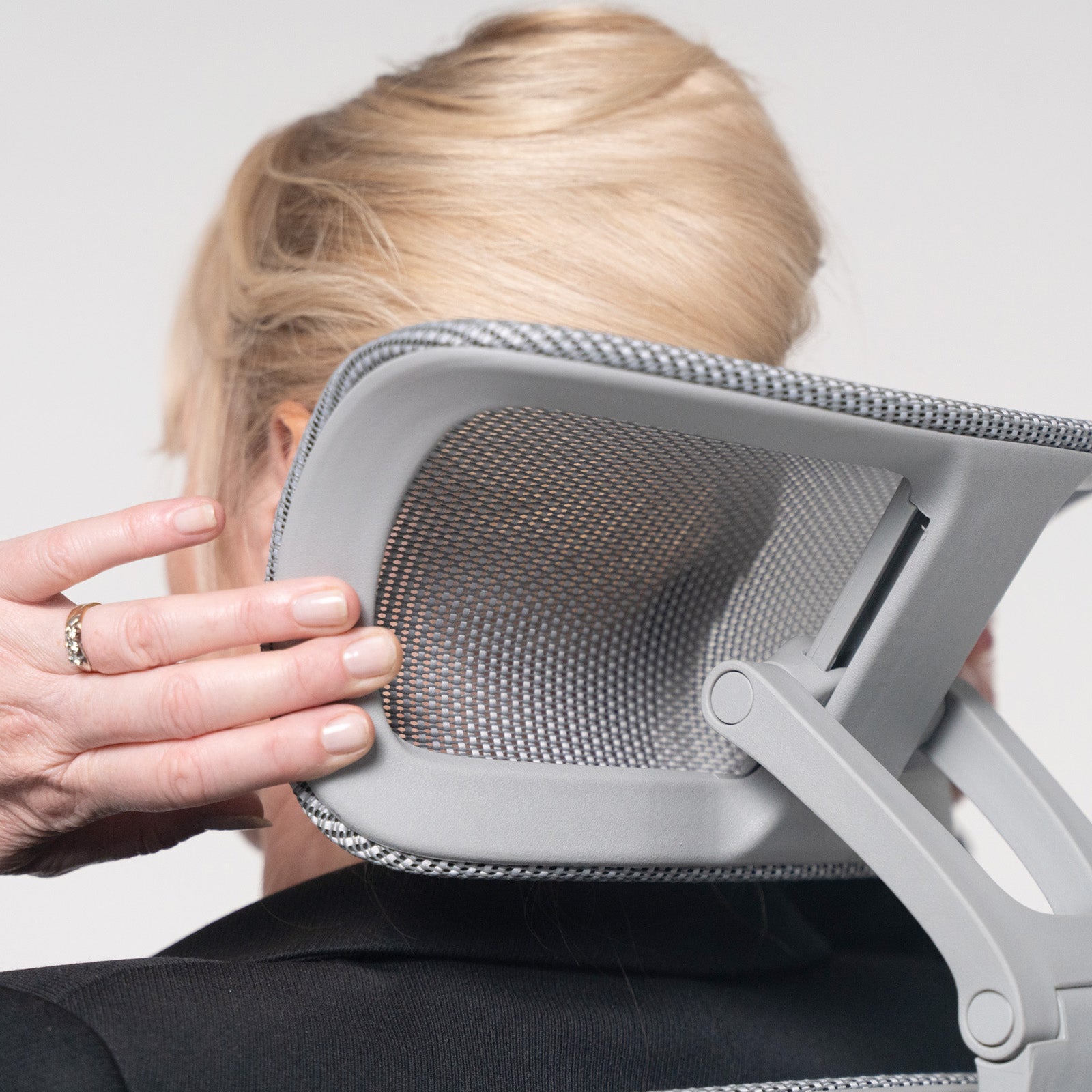 Close-up of a mesh ergonomic office chair headrest being adjusted by hand, demonstrating personalised neck and head support.