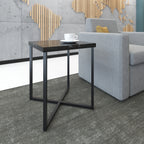 Small modern side table with black metal frame and dark top beside a lounge chair, styled with a coffee cup in a reception area.