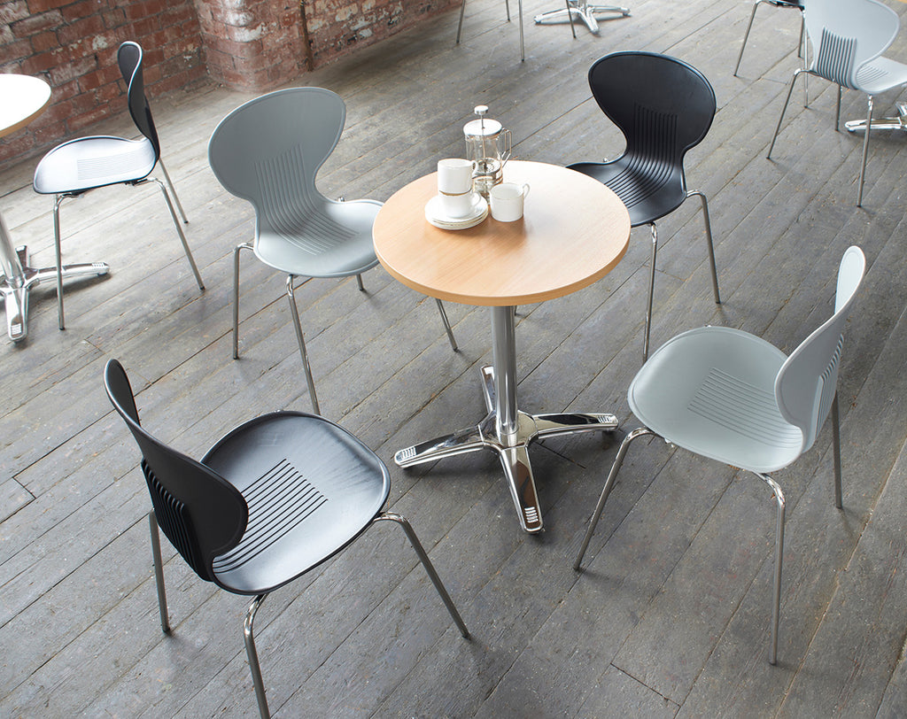 Modern chairs around a round wooden table on a wooden floor with a brick wall background.