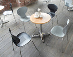 Modern chairs around a round wooden table on a wooden floor with a brick wall background.