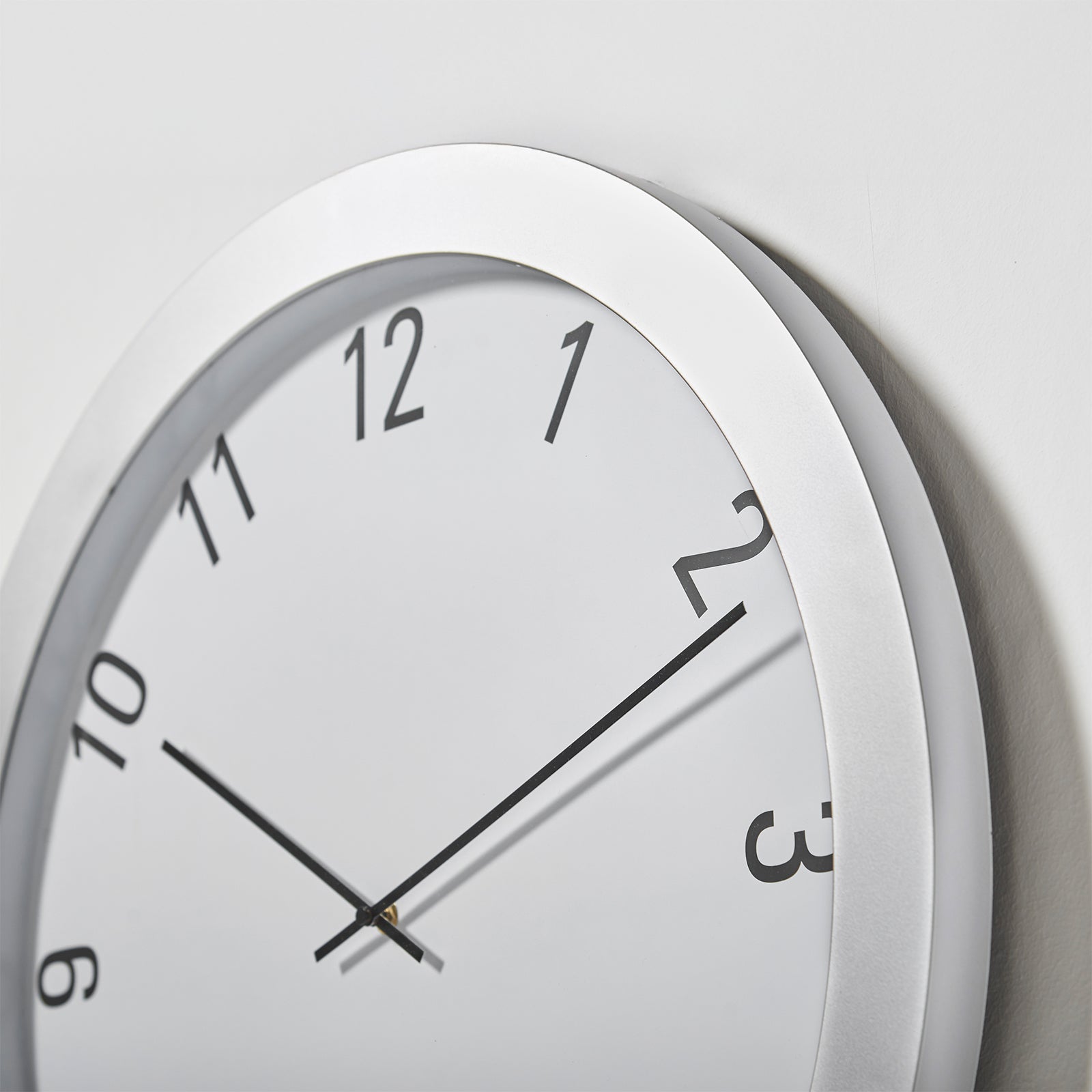 White wall clock close up with black numbers and hands on a light grey background