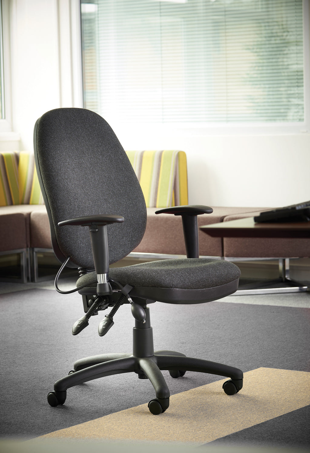 Grey office chair in a modern office setting with a couch and window blinds.