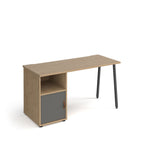 Office desk with oak-effect top, integrated storage cupboard with grey door and shelf, and black angled legs, shown against a white background.