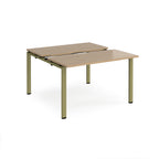 Two-person back-to-back office desk with oak-effect worktops and green metal legs, shown against a white background.