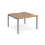 Two-person back-to-back office desk with oak-effect worktops and silver metal legs, designed for shared workspace layouts.