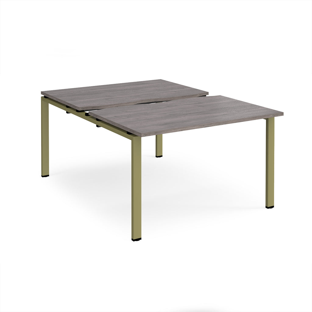 Large modular bench desk with a grey wood-effect top, integrated cable access slots, and green metal legs, shown on a white background.