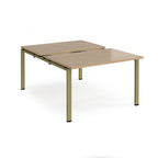 Large modular bench desk with a light oak wood-effect top, integrated cable access cut-outs, and green metal legs, shown on a white background.