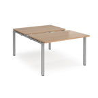 Large modular bench desk with a wood-effect top, integrated cable access cut-out, and silver metal legs, shown on a white background.