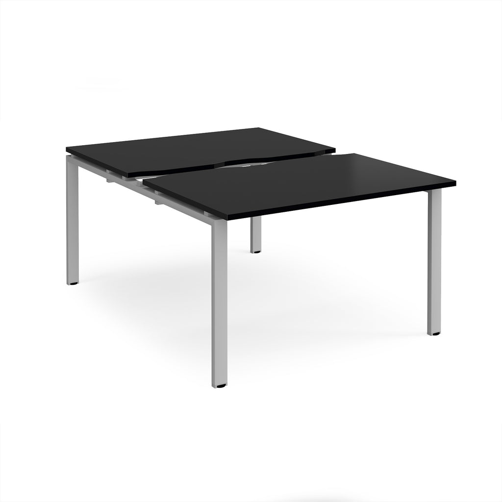 Large modular bench desk with a black top, integrated cable access cut-out, and silver metal legs, shown on a white background.